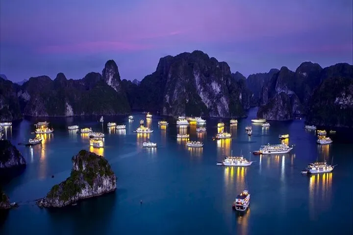 Cruise boats lit up at dusk among limestone islands on an overnight Ha Long Bay junk boat cruise, Vietnam