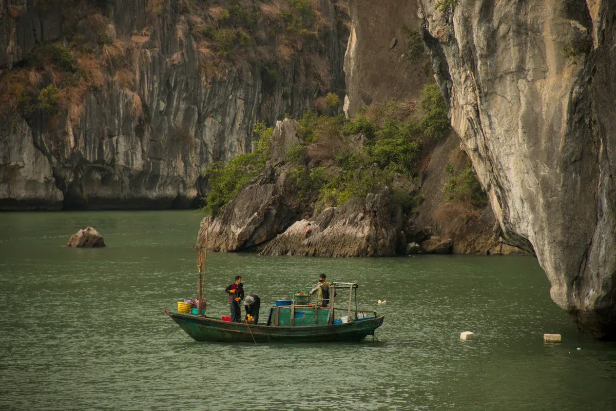 A small fishing boat below a karst cliff in Bai Tu Long Bay, the quietest water for a Ha Long Bay junk boat cruise