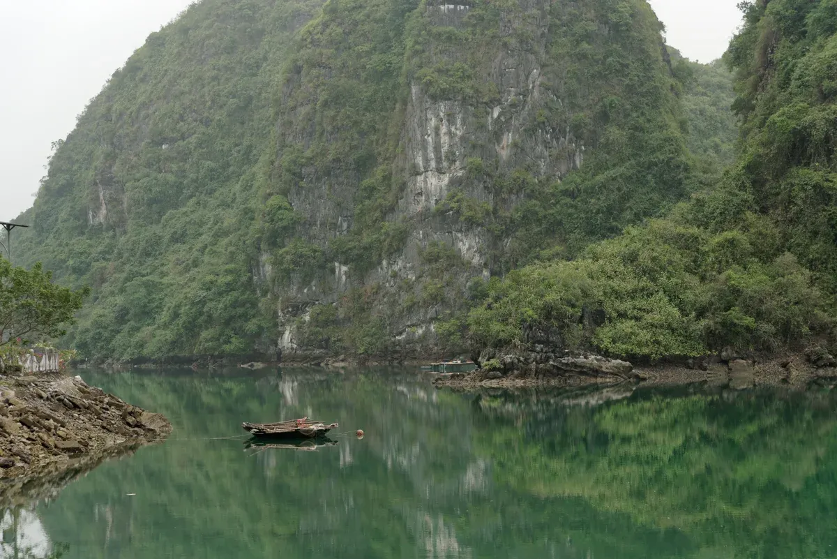 Green limestone cliff and a small boat on the southeast coast of Cat Ba Island, Halong Bay cruise