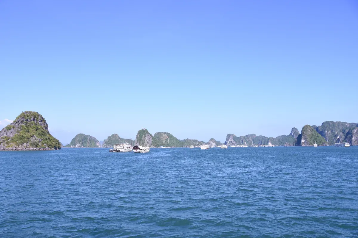 A cruise boat crossing blue water toward a line of karsts on a Ha Long Bay junk boat cruise